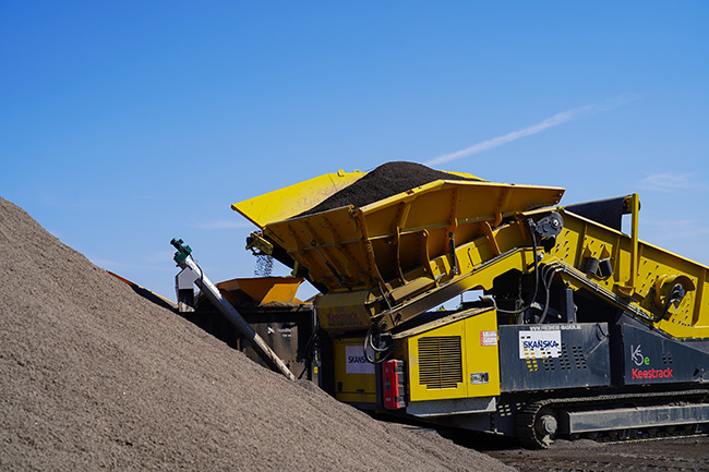 En stor hög med sand och maskinen som rengör sanden mot blå himmel. 